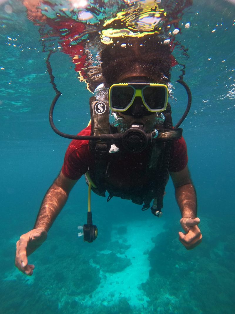 A diver just below the surface, facing the camera in mask and regulator with a camera clipped to the chest