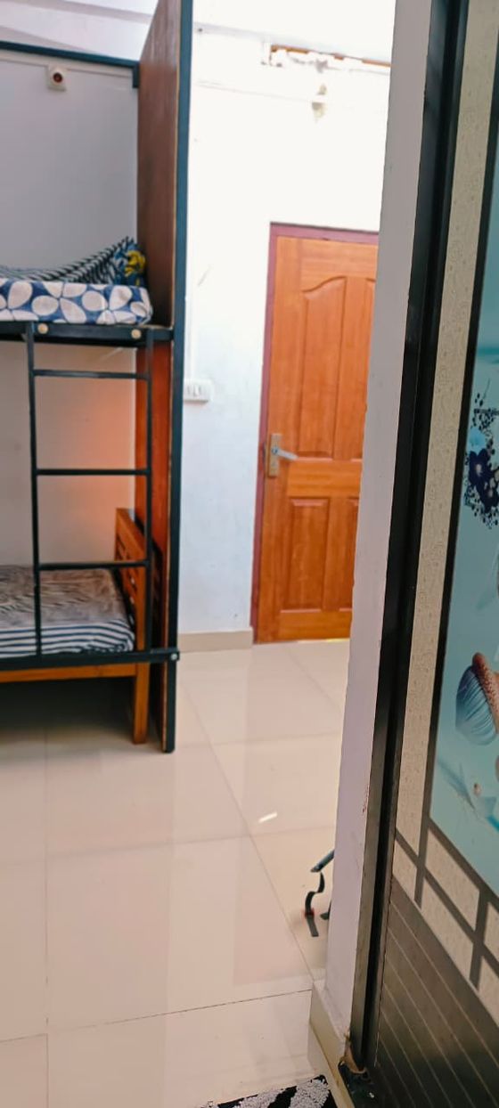 A bunk bed beside the dormitory's wooden door, on a tiled floor