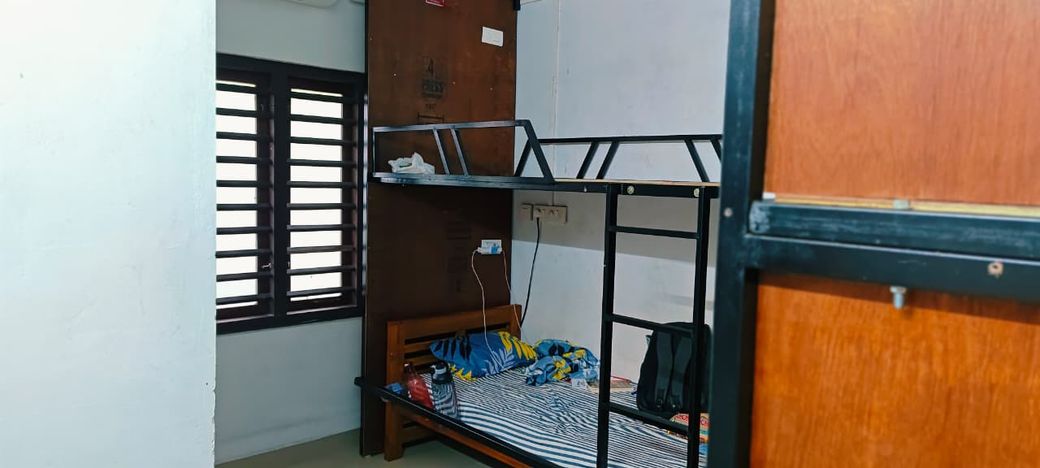 The AC dormitory: metal bunk beds with striped mattresses beside a window with wooden louvres