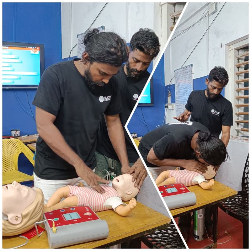 Two Lak Scuba instructors practising infant CPR on a manikin beside an AED trainer, one giving rescue breaths
