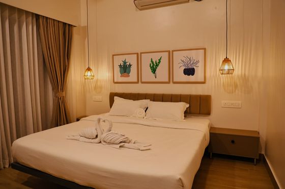 A Premium beach AC room: a double bed with towels folded into swans, two pendant lamps and three framed plant prints above the headboard