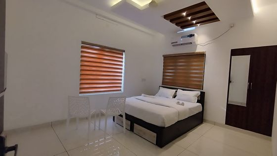 Another Standard AC room: a double bed with white linen, two chairs by the window, a wardrobe and a wall-mounted air conditioner
