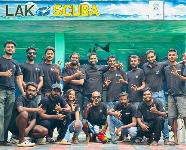 Around fifteen Lak Scuba instructors, divemasters and crew grouped outside the dive centre beneath its LAK SCUBA sign and PADI Five-Star plaque